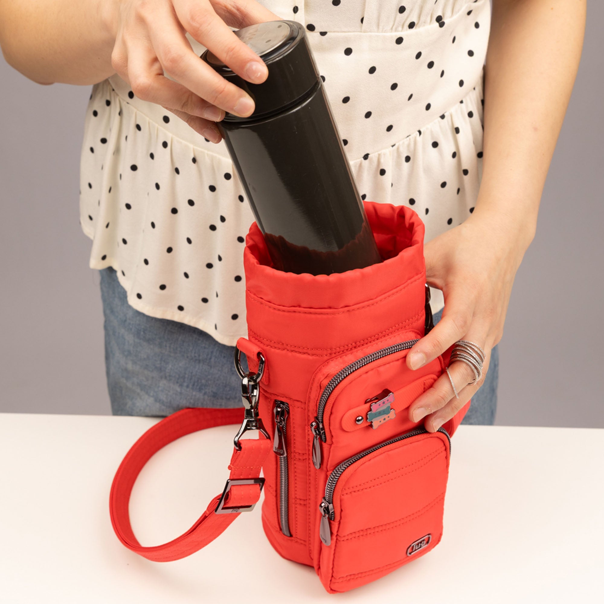 Lug Huggie Wide crossbody water bottle holder with charm bar in cayenne red, shown with water bottle and accessories.